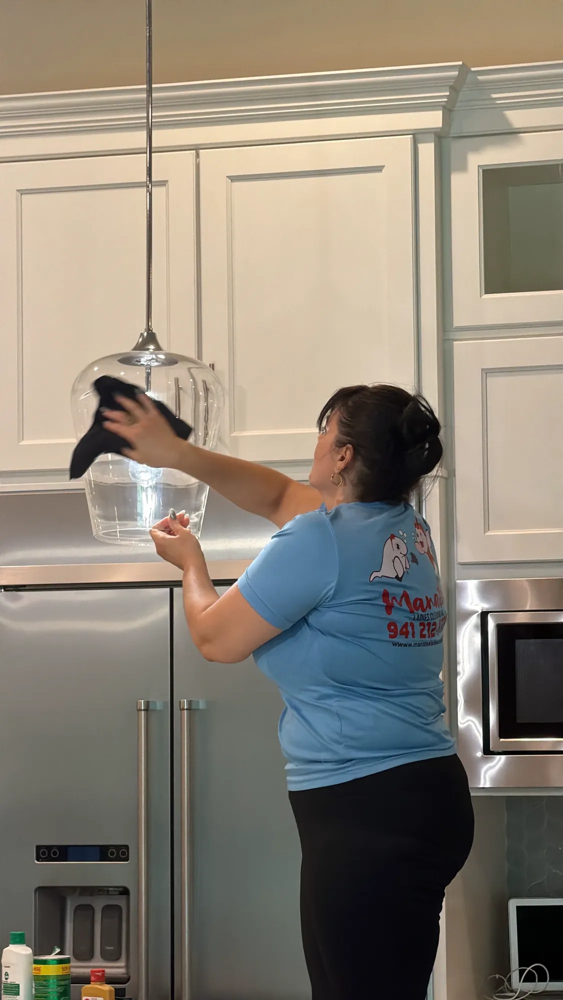 Manatee Ladies crew member dusting a glass pendant light fixture in a luxury kitchen