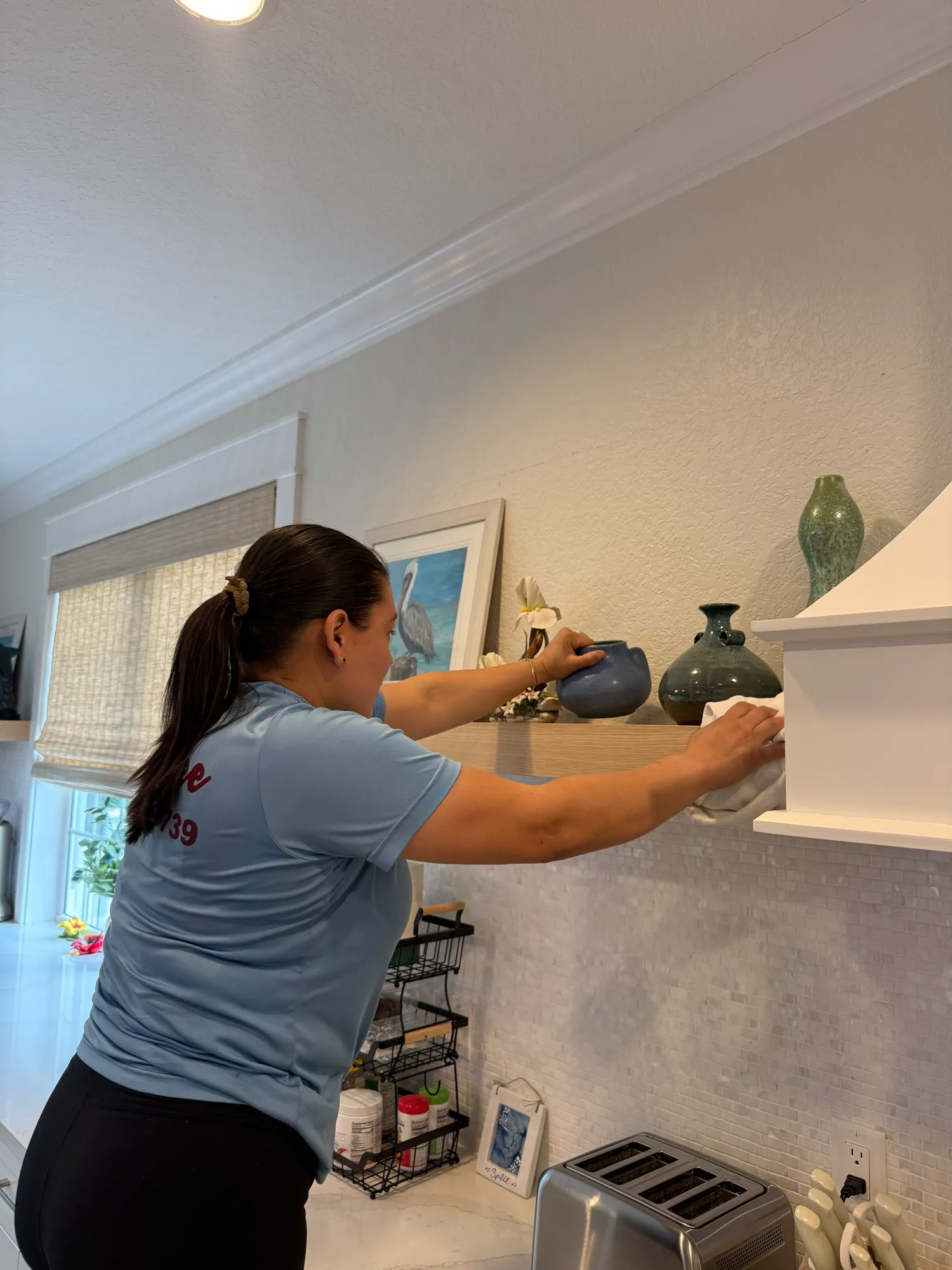 Cleaner carefully dusting decorative vases on a floating shelf